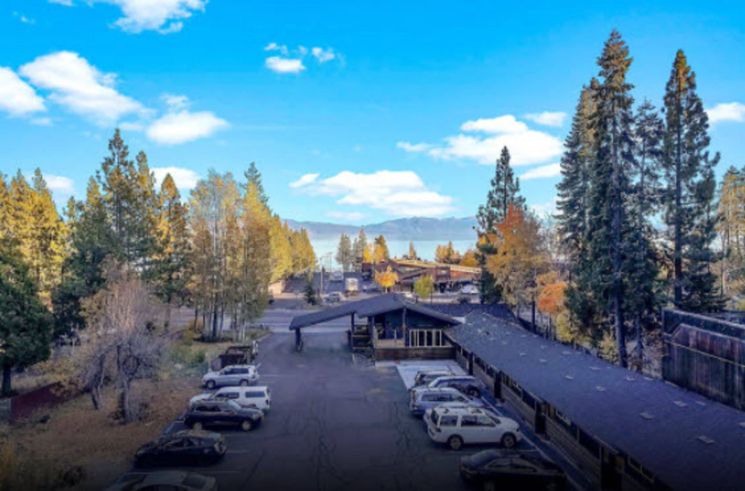 A parking lot with several cars, a covered building, and tall trees in the background.