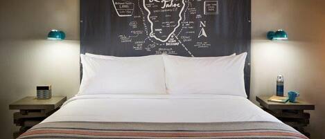 A hotel room with a bed, a map of Lake Tahoe on the wall, and two nightstands with lamps.