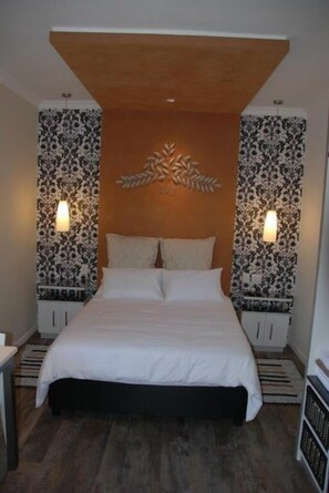A bedroom with a bed, two nightstands, a decorative wall piece, and patterned wallpaper.