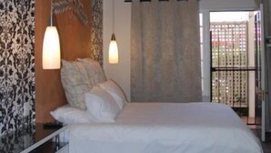Een slaapkamer met een groot bed, twee hanglampen, een houten plafond en uitzicht door een glazen deur.