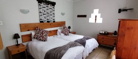 A bedroom with two beds, a ceiling fan, a wall-mounted light, a wooden headboard, a small wooden nightstand, a dresser, and a window with a view.
