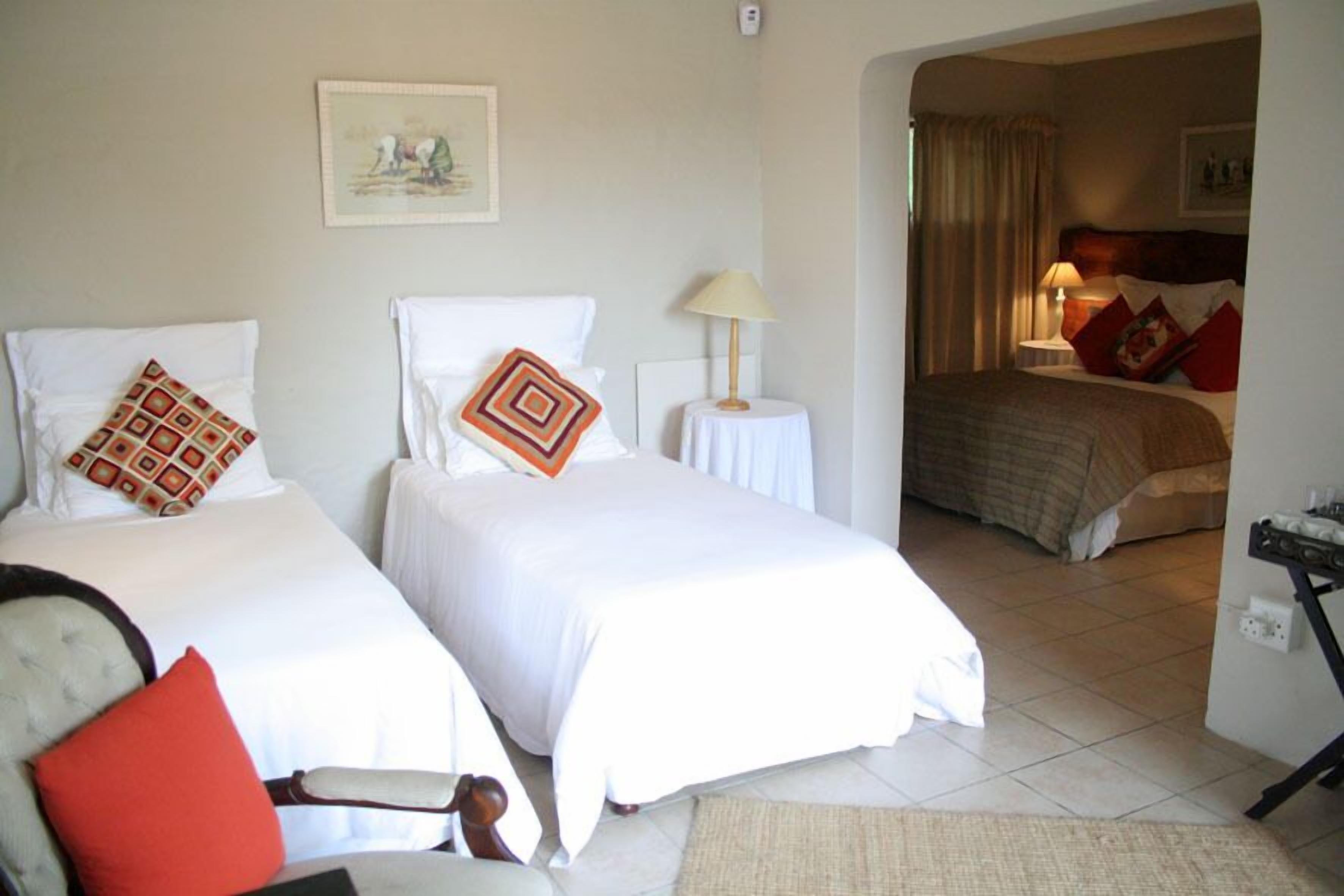 A hotel room with two beds, a chair, a small table, and a lamp.