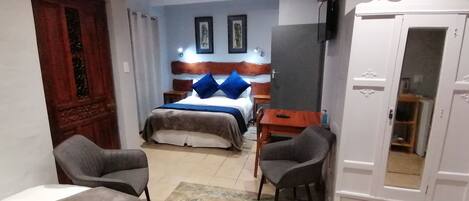 A hotel room with a bed, two chairs, a wardrobe, and a small table.