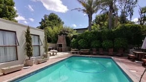 Et rektangulært pool med flisekant, omgivet af en patio med udendørs møbler og plantekasser.