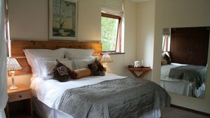 En pænt redt seng med et gråt tæppe, et træsengegærde og et sengebord med en lampe.