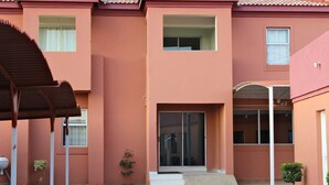 A building with a red exterior, a covered entrance, and a small garden area with plants. - Mogwase Bed and Breakfast (Moses Kotane)