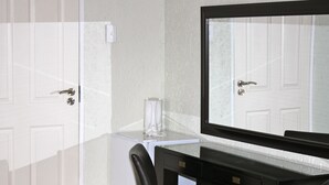 A hotel room with a white door, a small white table with a glass container, a black desk, and a large mirror. - Mogwase Bed and Breakfast (Moses Kotane)