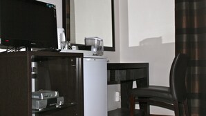 A hotel room with a flat-screen TV, a coffee maker, a refrigerator, a glass cabinet with electronic devices, a wooden chair, and a large mirror. - Mogwase Bed and Breakfast (Moses Kotane)