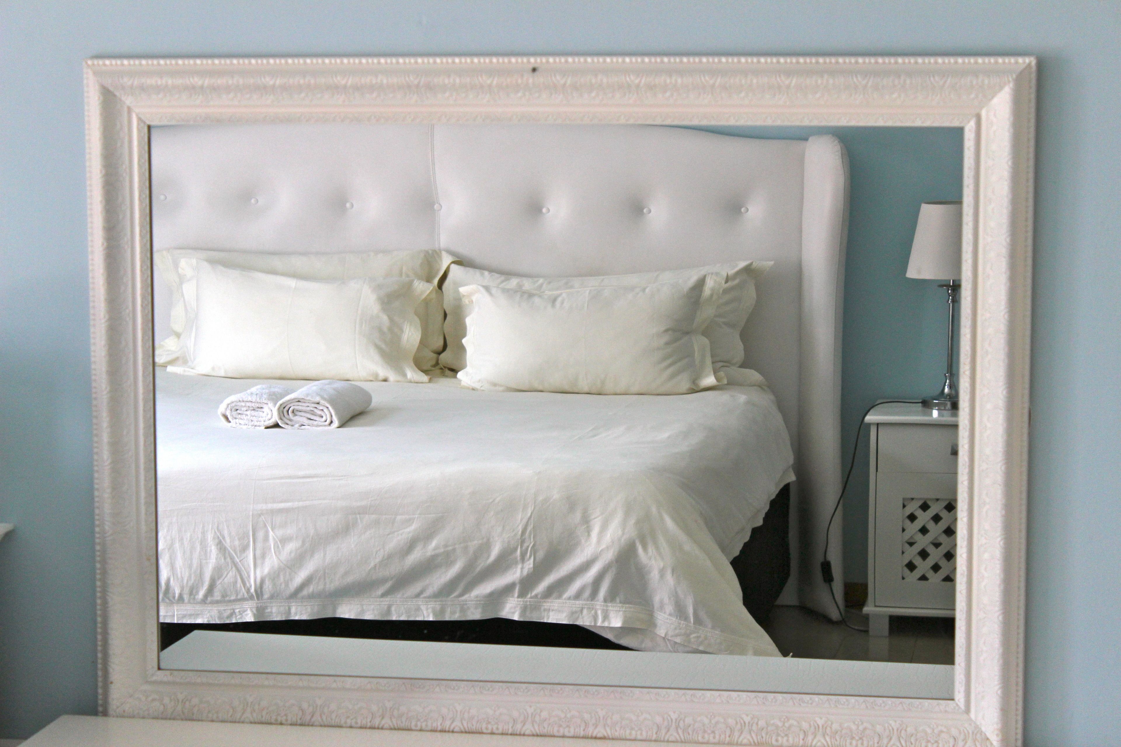 A neatly made bed with white linens and pillows, a white headboard, and a small bedside table with a lamp.