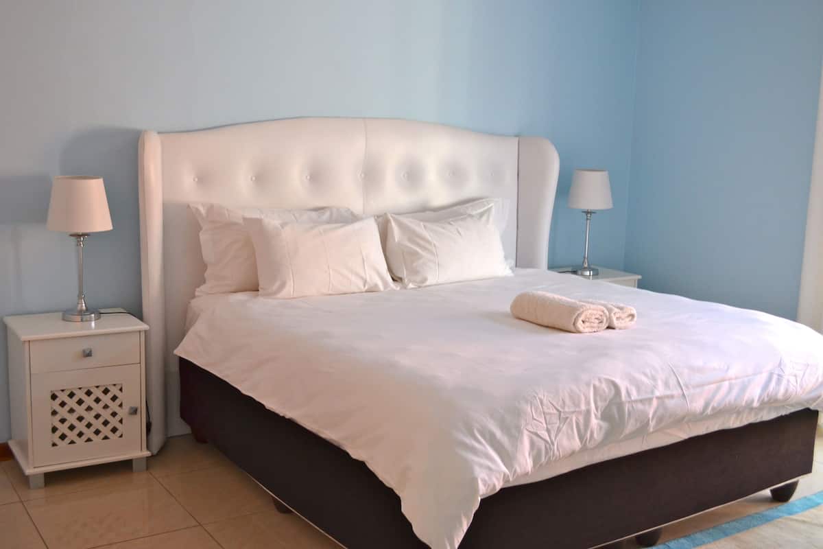 A neatly made bed with white linens and a rolled towel, flanked by two bedside tables with lamps, in a room with light blue walls.