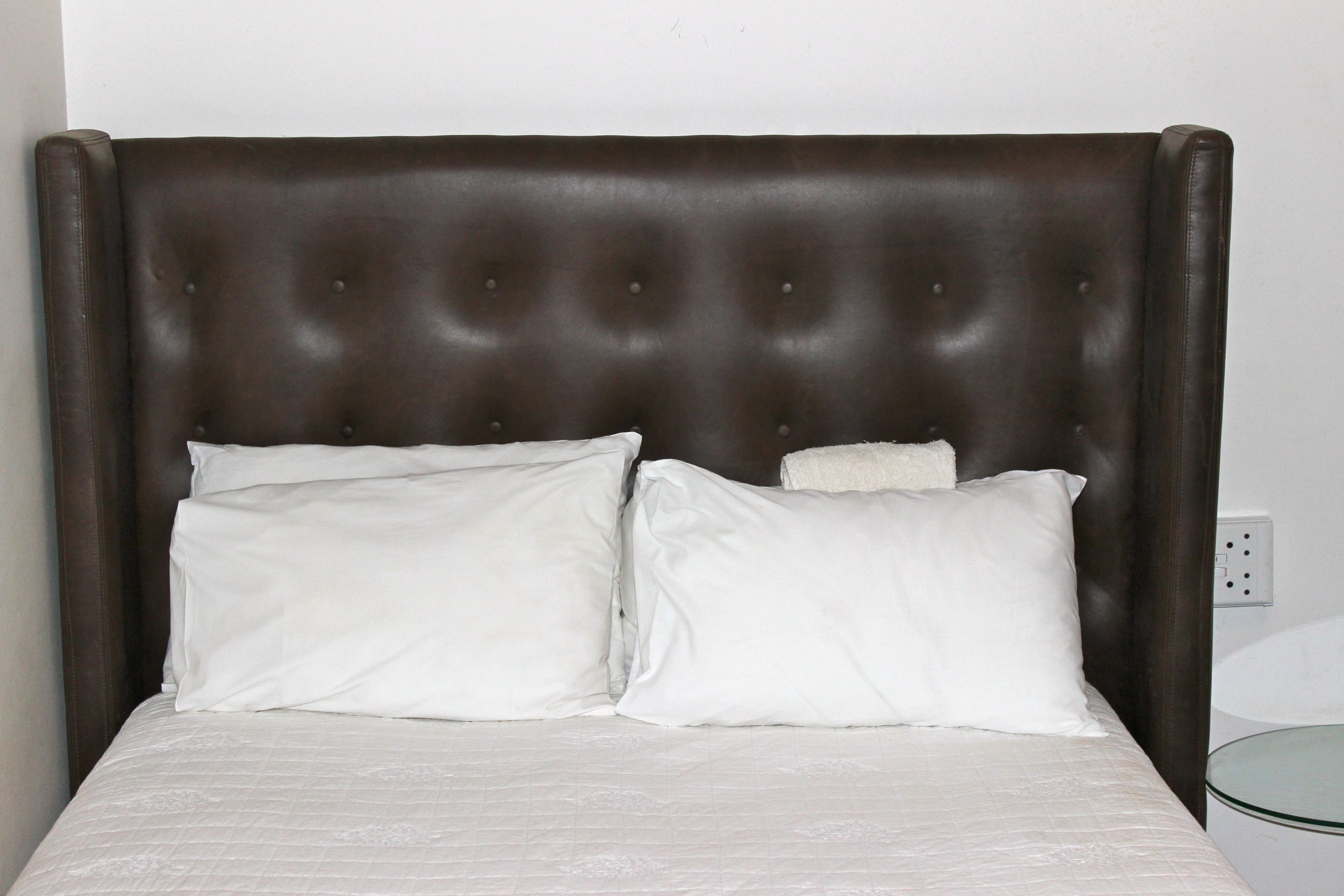 A bed with a tufted headboard, two white pillows, and a white bedspread.