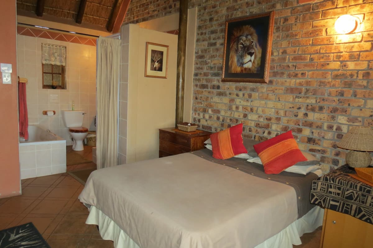 Ein Schlafzimmer mit einem großen Bett, einer Ziegelwand, einem Gemälde eines Löwen und einem durch eine offene Tür einsehbaren Badezimmer.
