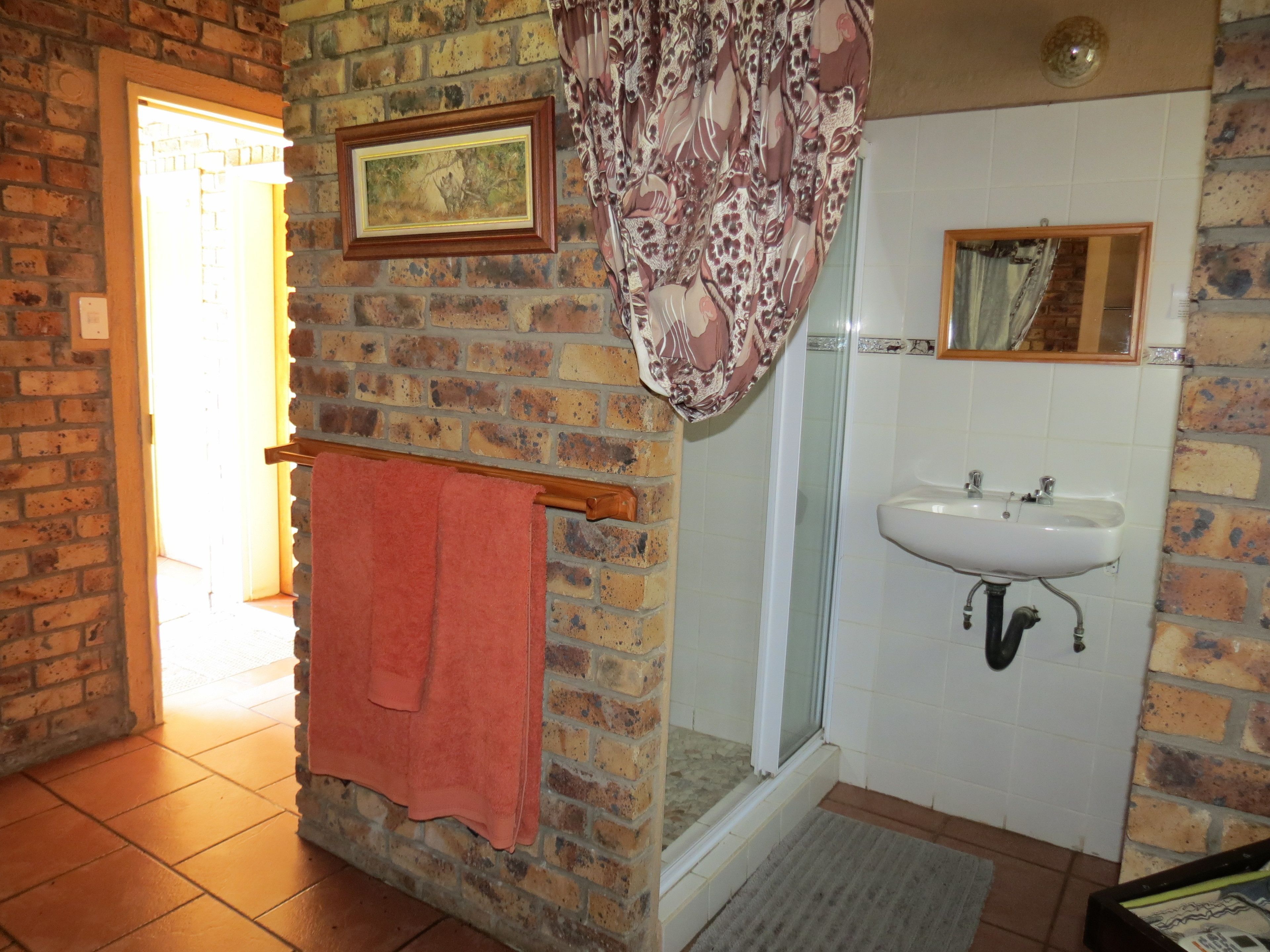 A bathroom with a brick wall, a shower, a sink, and a towel rack.