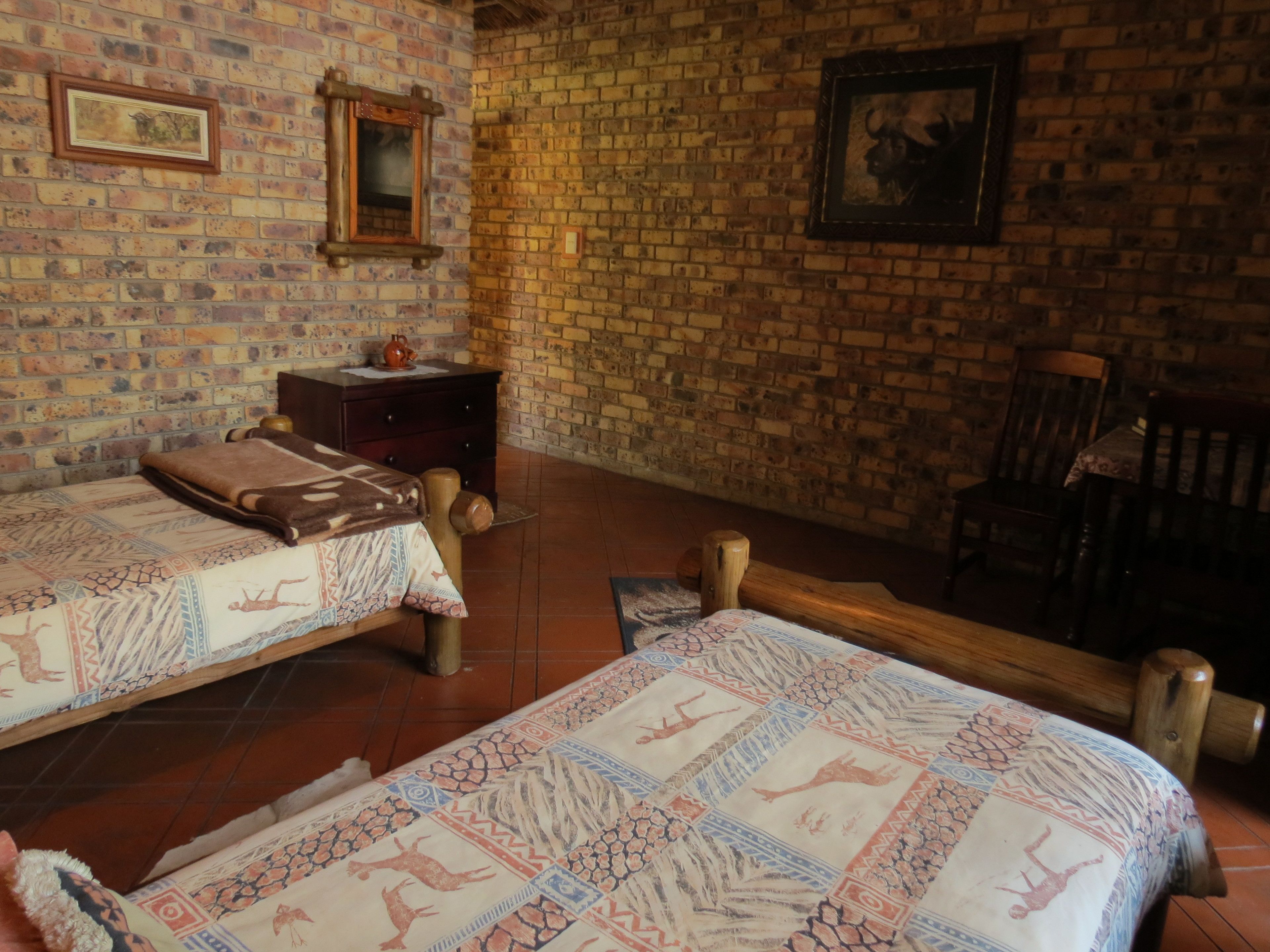 A room with two beds, a wooden nightstand, a small table, and a brick wall with framed pictures.