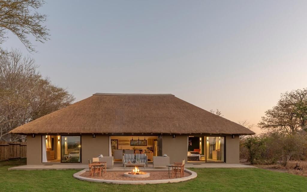 A modern house with a thatched roof, a fire pit, and a patio with seating.