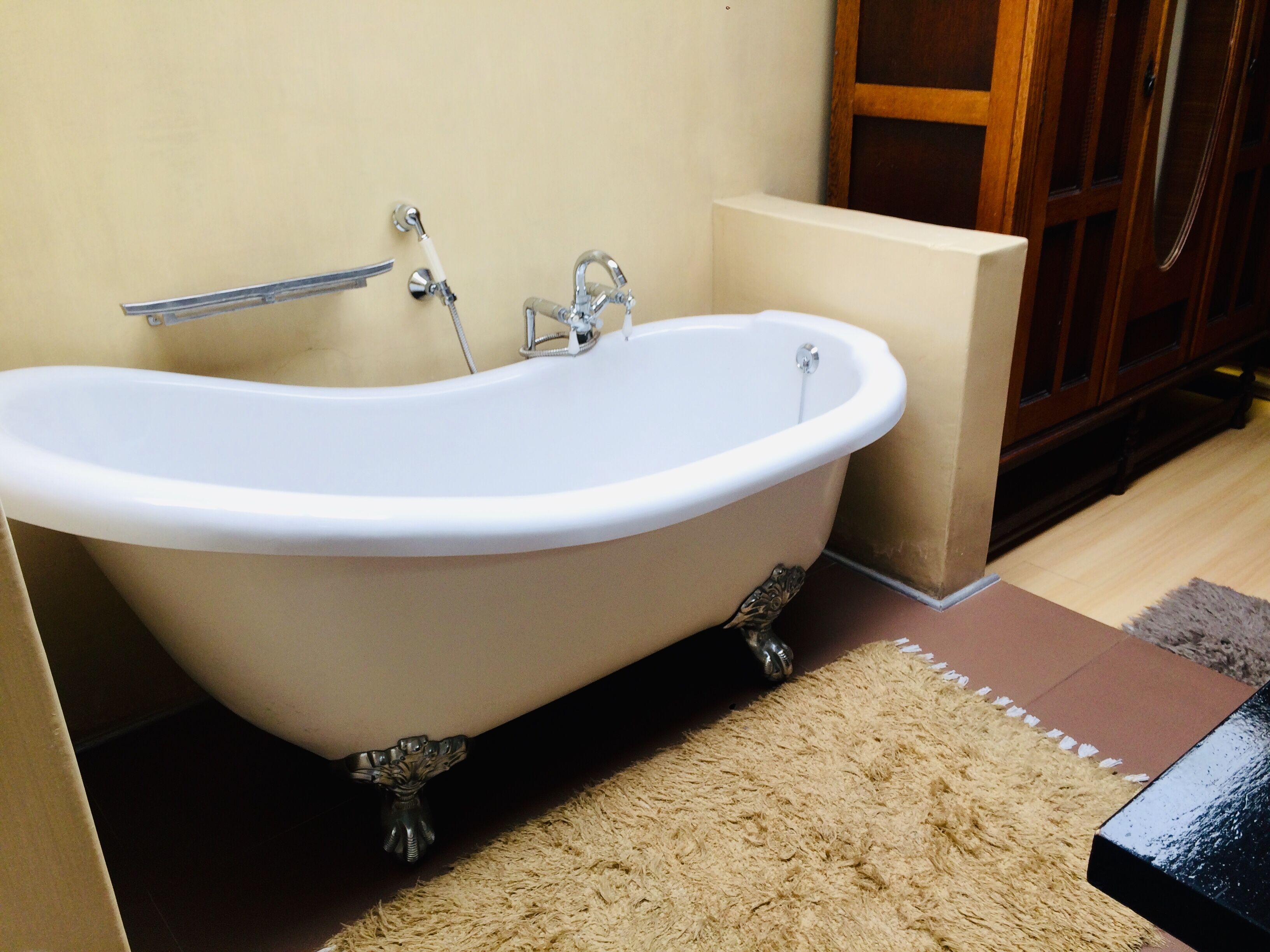 A freestanding bathtub in a bathroom with a wooden cabinet and a beige rug.