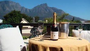 A table with a bottle of champagne, a wine glass, and a bucket, set against a scenic mountain backdrop.