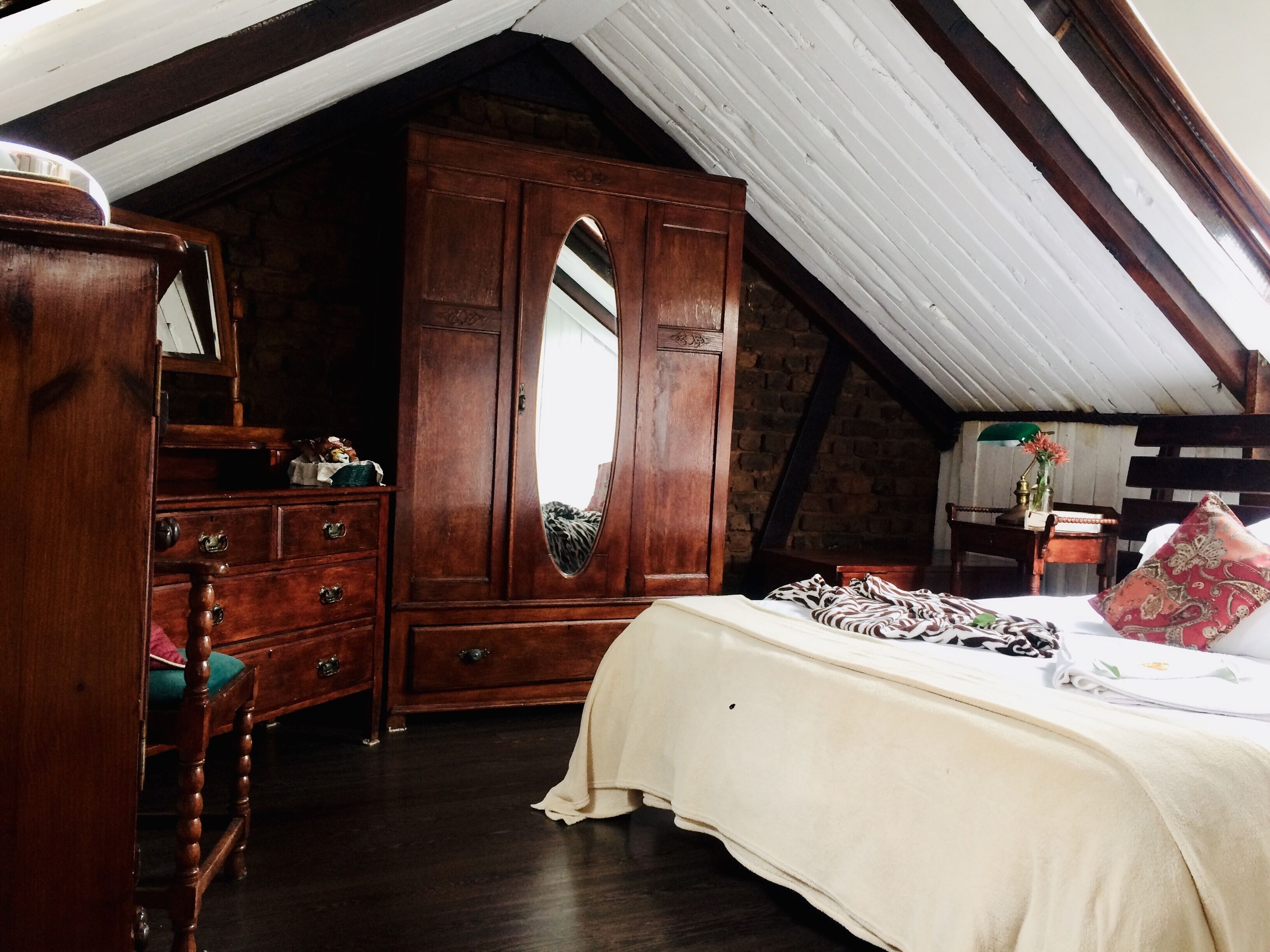 A bedroom with a large wooden wardrobe, a bed with a white bedspread, and a mirror above the wardrobe.
