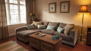 A living room with a sectional sofa, a wooden coffee table, and a floor lamp. There are two framed pictures on the wall and a vase with flowers on a side table.