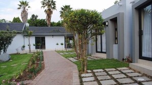 Une maison moderne avec un chemin piétonnier dallé, un petit jardin et des palmiers.