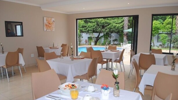 Un espace repas avec des tables préparées pour le petit-déjeuner, une vue sur la piscine et une grande fenêtre.