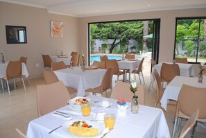 Uma área de refeições com mesas preparadas para o café da manhã, vista para a piscina e uma janela grande.