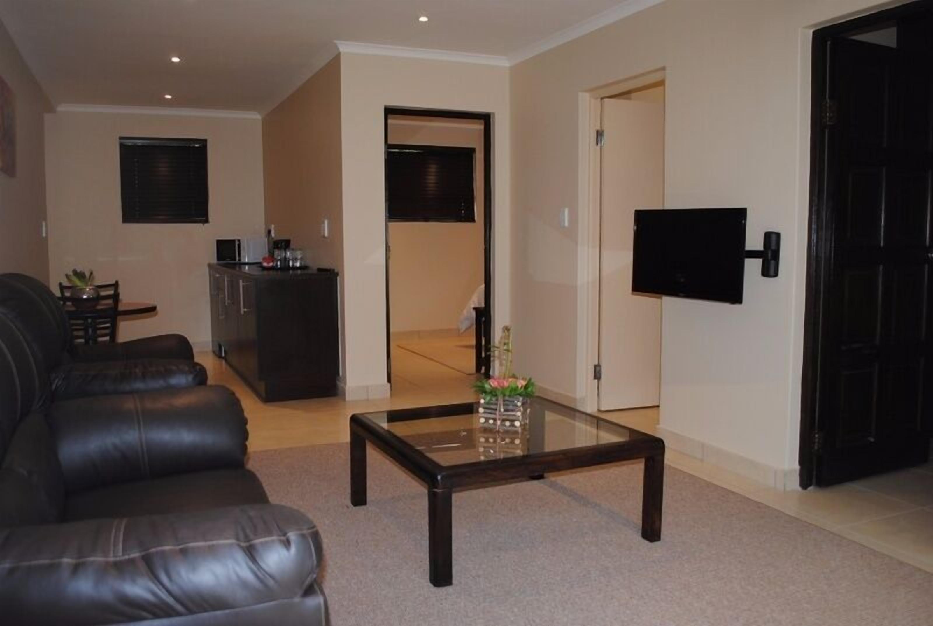 A living room with a leather sofa, a glass coffee table, and a flat-screen TV mounted on the wall.