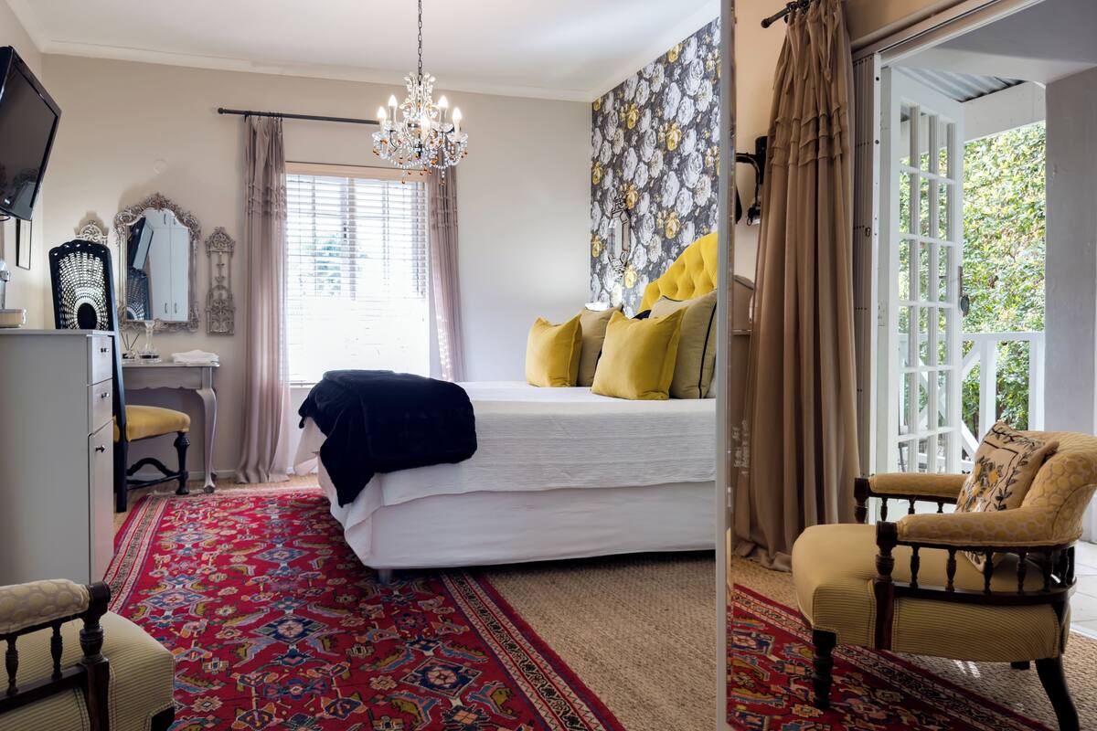 A bedroom with a large bed, a desk, a chair, a chandelier, and a view through an open door.