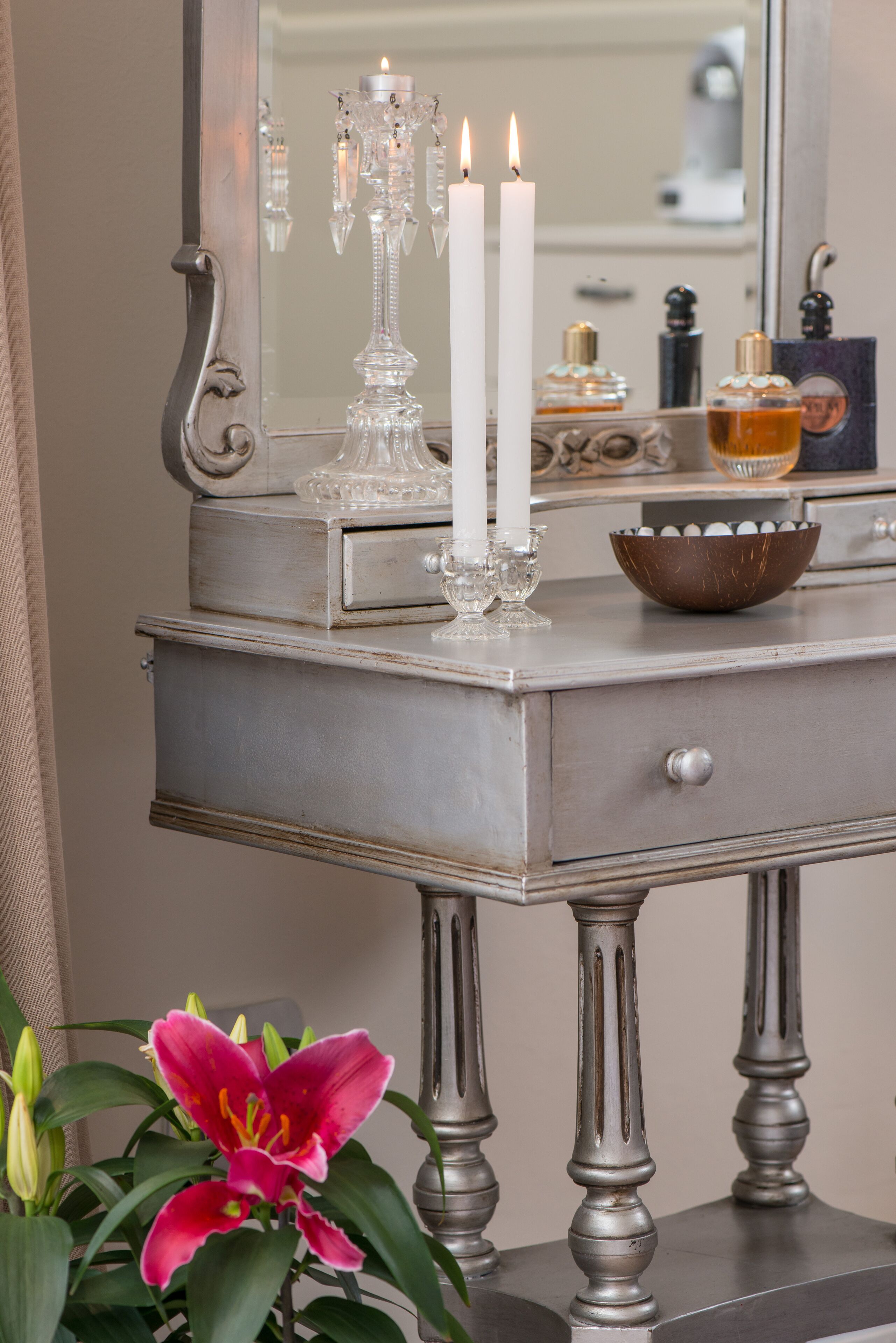 A vintage-style vanity with a mirror, two lit candles, a glass bowl, and a potted plant.