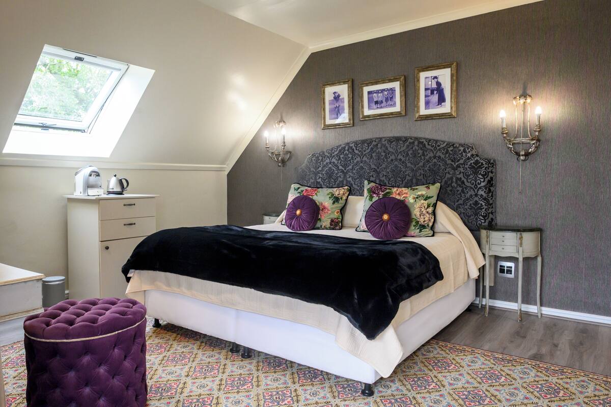 A bedroom with a bed, a window, a nightstand, a lamp, and a patterned rug.