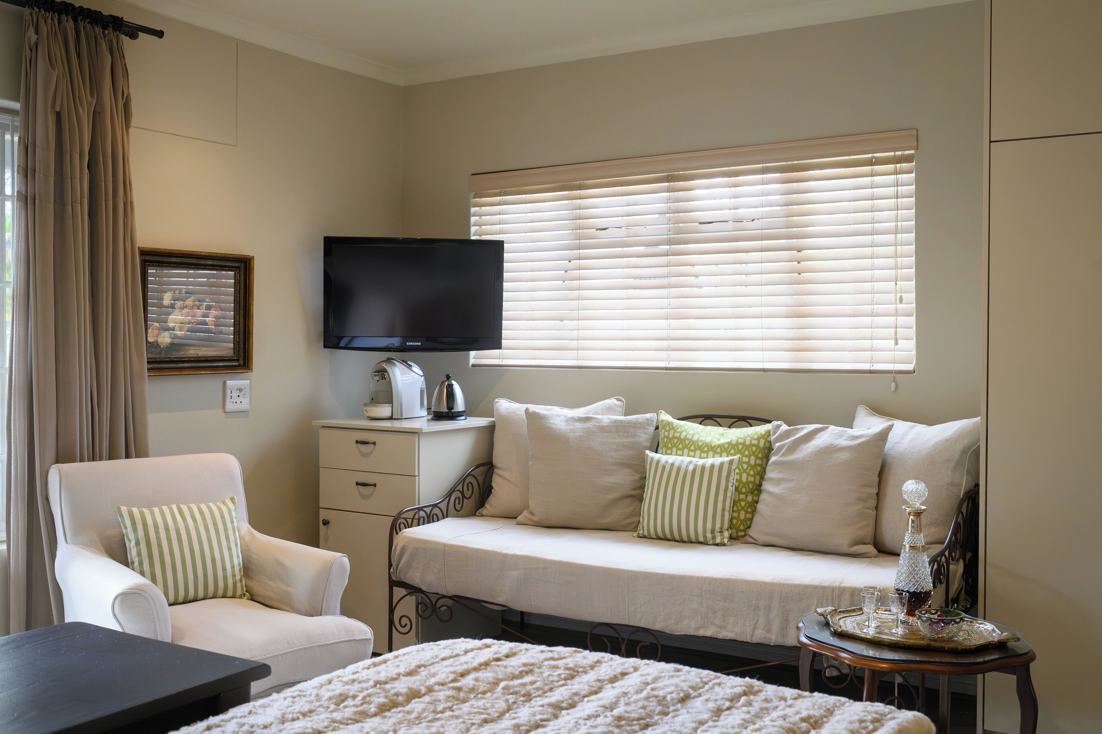 A bedroom with a bed, a chair, a TV, a bedside table, and a window with blinds.