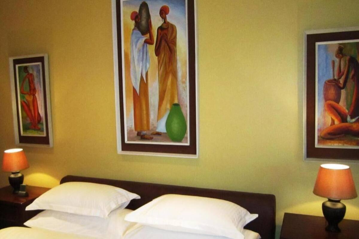 A hotel room with a bed, two wall-mounted lamps, and three framed artworks.