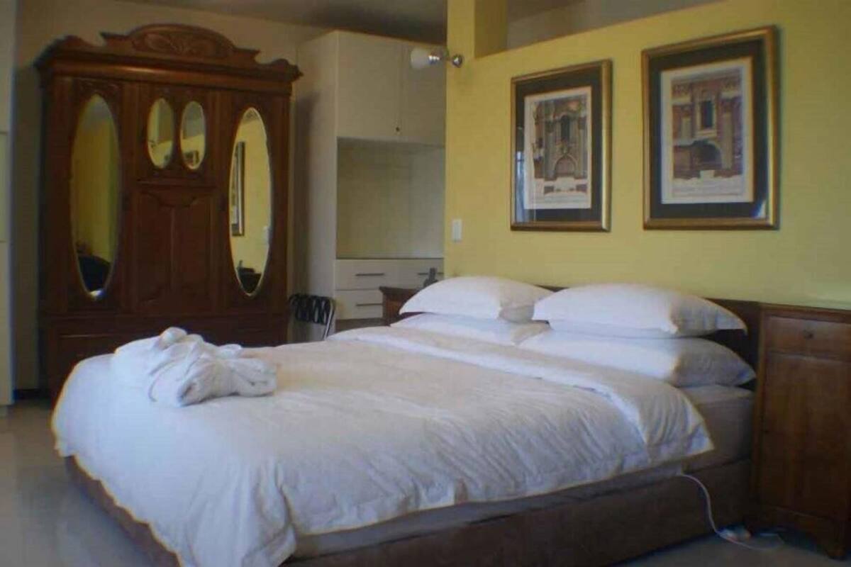 A bedroom with a large bed, wooden wardrobe, and two framed pictures on the wall.