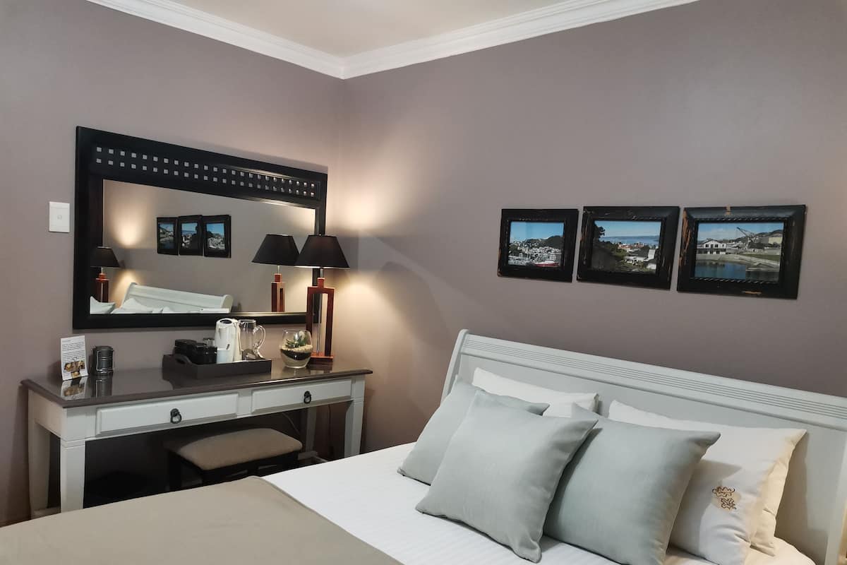Une chambre d’hôtel avec un lit, un bureau doté d’une lampe, un miroir et trois tableaux encadrés accrochés au mur.