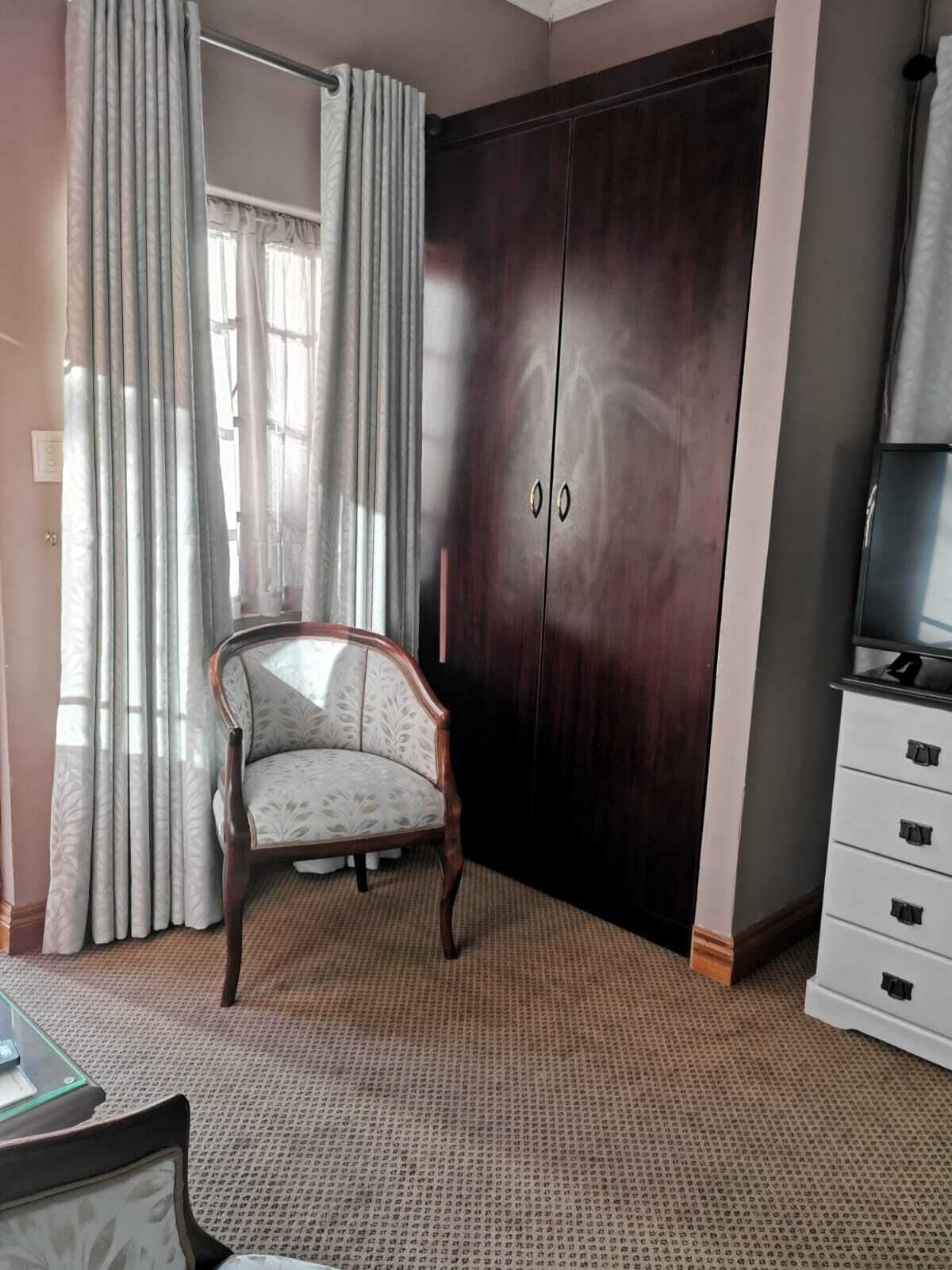 A room with a dark wooden wardrobe, a white upholstered chair, and a television on a stand.