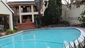 A swimming pool with a curved edge, surrounded by a patio area with outdoor furniture and plants. - 2 Leafed Doors (Sandton)