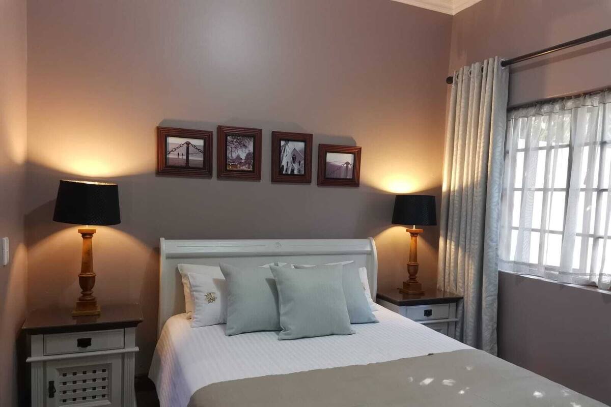 Un lit bien fait, avec une tête de lit blanche, deux tables de chevet avec des lampes et trois tableaux encadrés accrochés au mur.