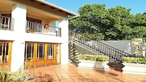 A two-story building with a balcony on the upper floor, a staircase with a metal railing, and a potted plant in the foreground. - 2 Leafed Doors (Sandton)