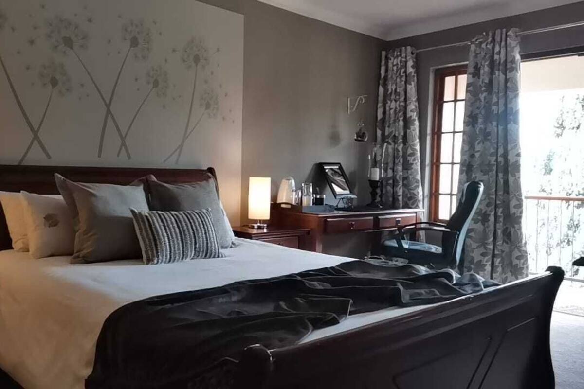 Une chambre d’hôtel avec un grand lit, un bureau avec une chaise, une fenêtre avec des rideaux et un mur orné d’un motif floral.