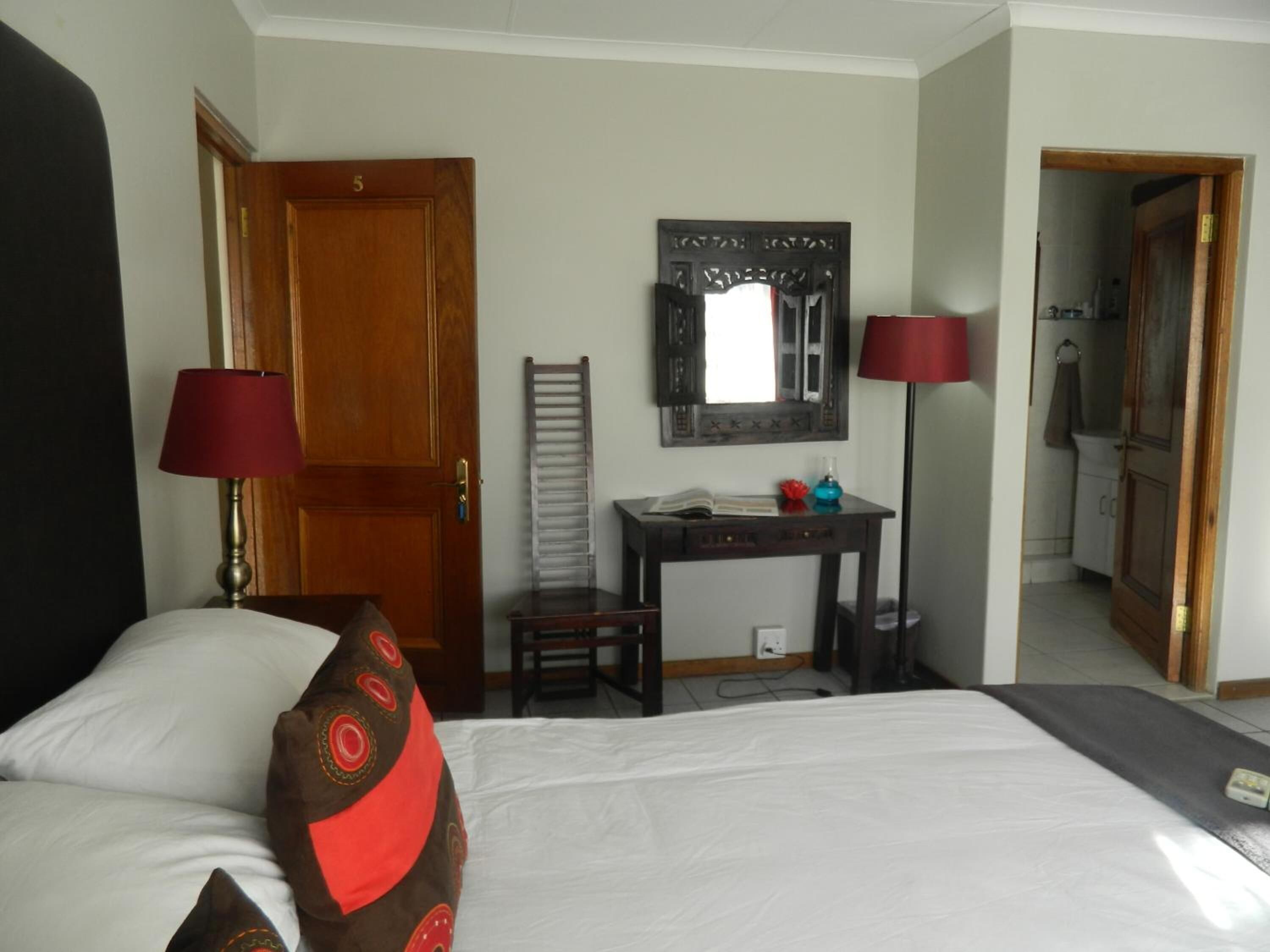 A hotel room with a bed, a desk, a mirror, and a door.