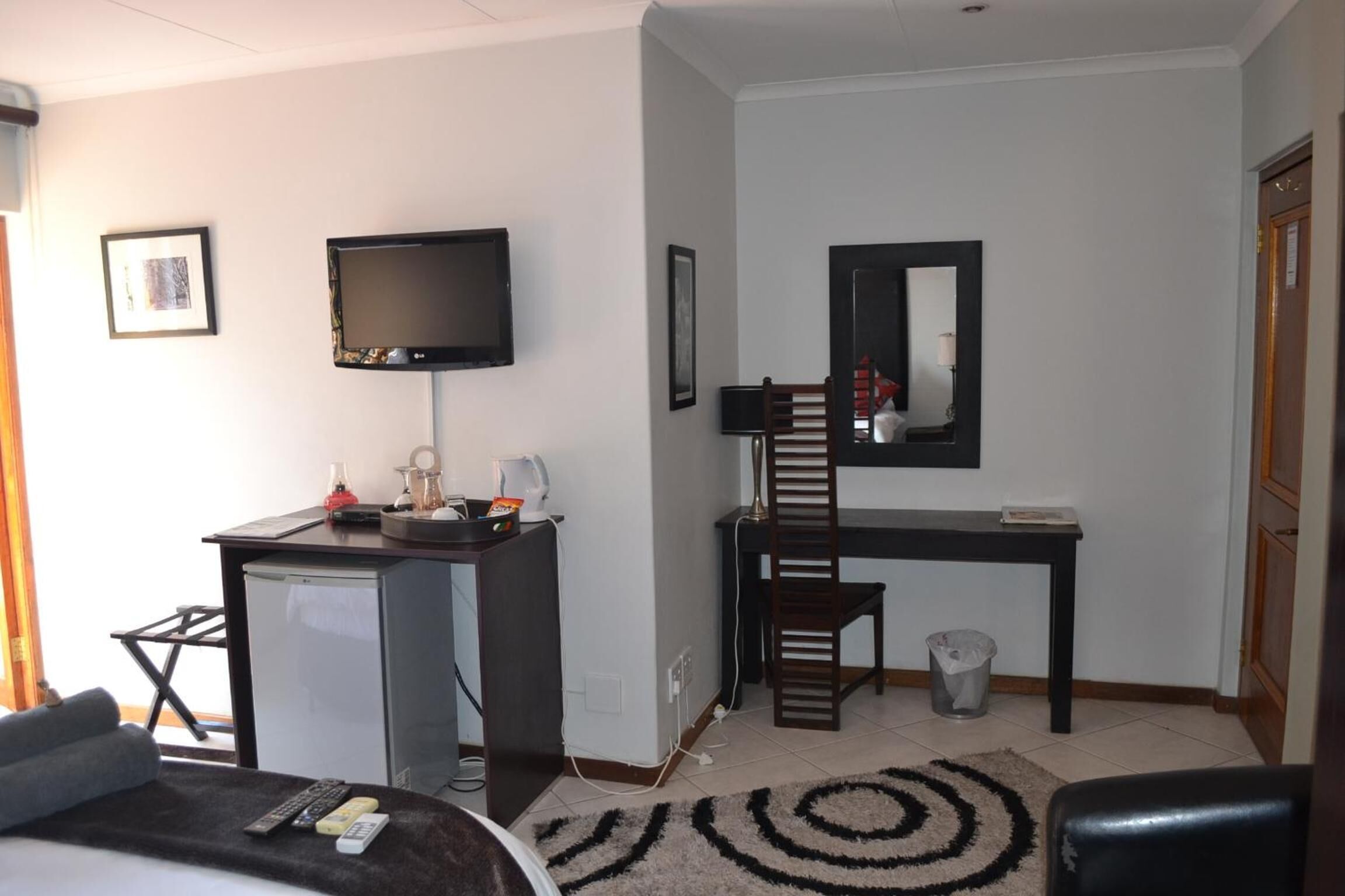 Une chambre d’hôtel équipée d’un bureau, d’une télévision, d’une chaise, d’un petit réfrigérateur, d’une poubelle et d’un lit.