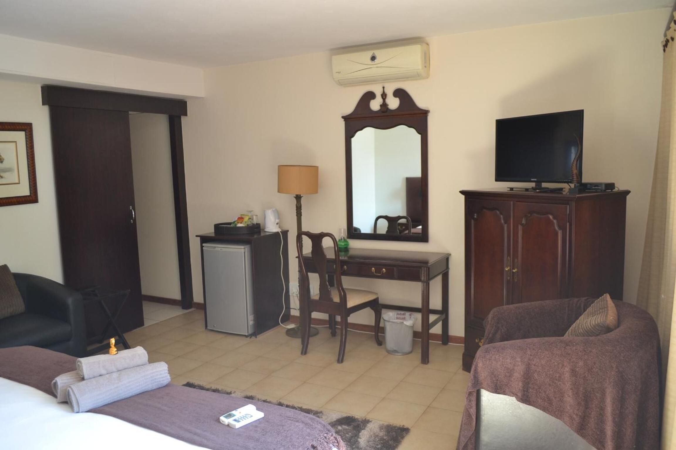 A hotel room with a bed, a desk with a computer, a television, a chair, and a cabinet.