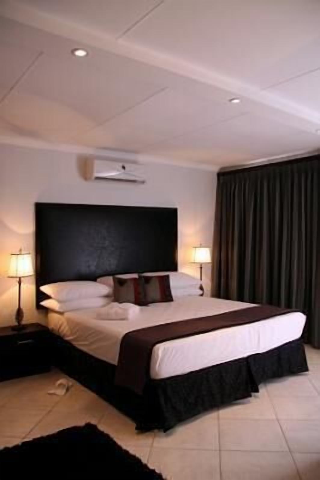 Ein Hotelzimmer mit einem großen Bett, zwei Nachttischlampen, einem dunklen Kopfteil und einem Fenster mit Vorhängen.