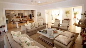 A spacious living room with a sofa set, a coffee table, and a dining area with a kitchen in the background. - Fairlight Beach House (eMdloti)