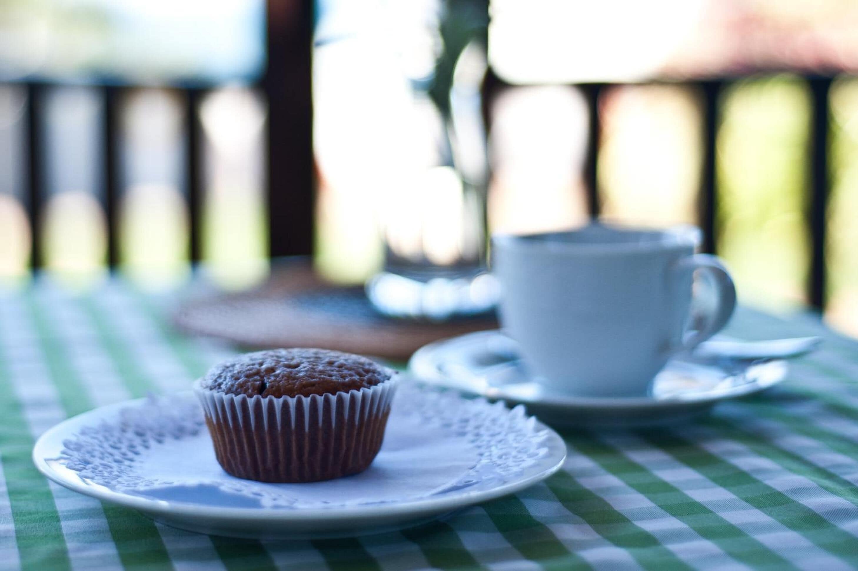 A muffin on a plate with a cup on a table.