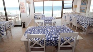 A dining area with tables and chairs, large windows with a view of the beach, and a ceiling fan. - Fairlight Beach House (eMdloti)