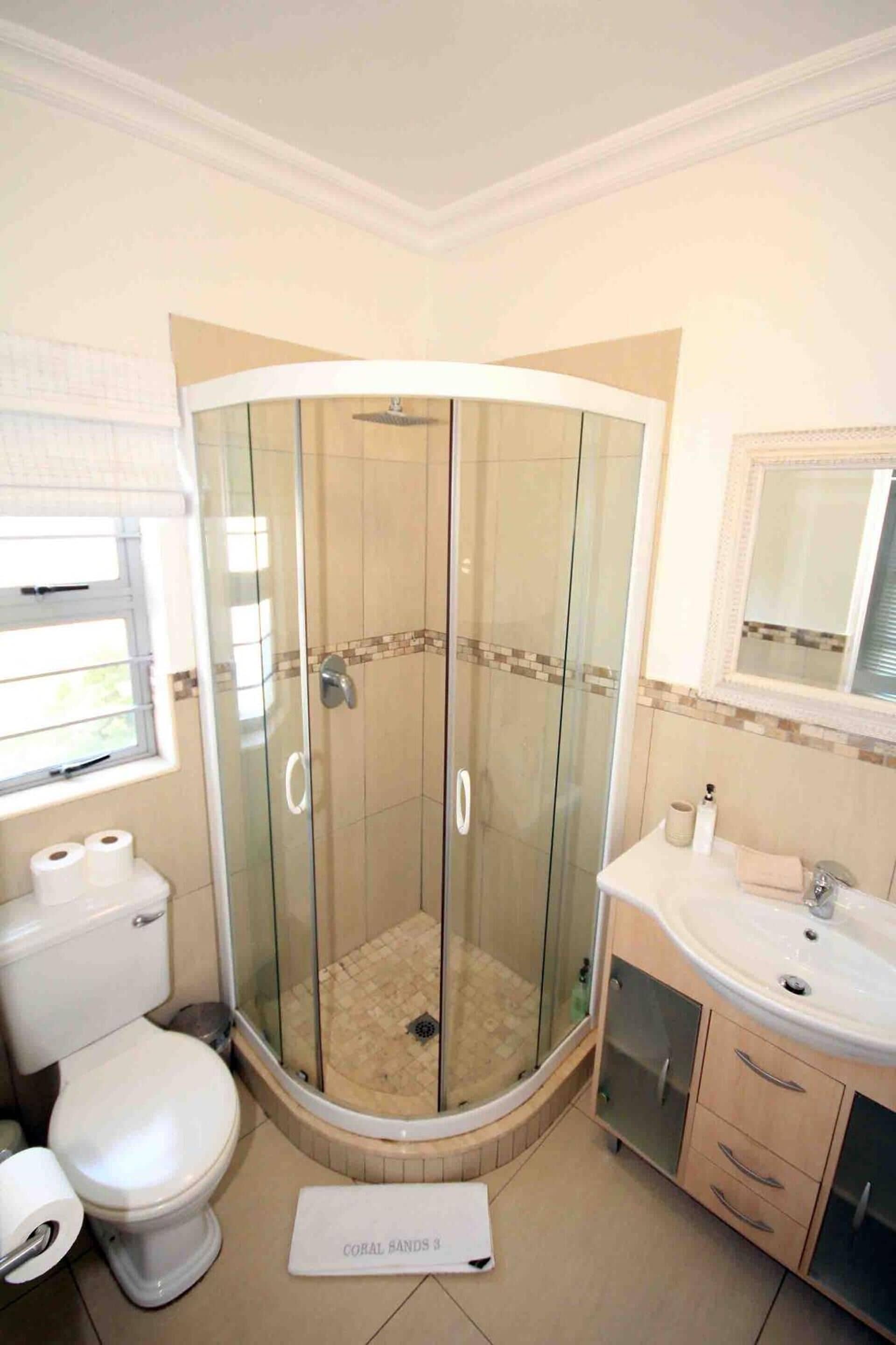 Une salle de bain avec une douche à parois de verre, des toilettes, un lavabo et un miroir.