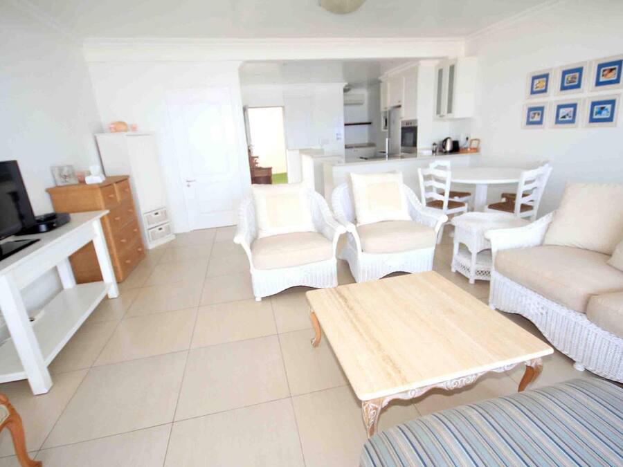 Un salón amplio con televisión, muebles de mimbre blanco, una mesa de centro de madera y un comedor con una mesa y sillas blancas.