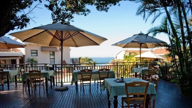 An outdoor dining area with tables and chairs, large umbrellas, and a view of the sea. - Fairlight Beach House (eMdloti)