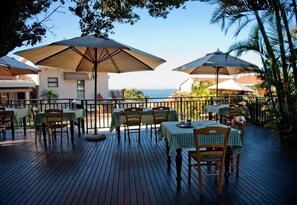 An outdoor dining area with tables and chairs, large umbrellas, and a view of the sea. - Fairlight Beach House (eMdloti)